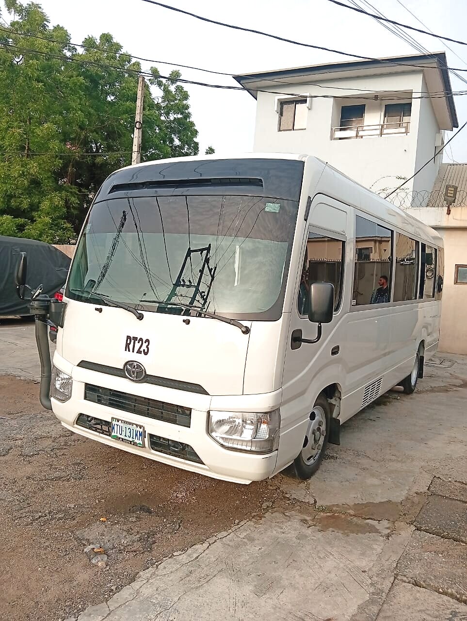 White Toyota Coaster bus parked in a Lagos compound, front three-quarter view