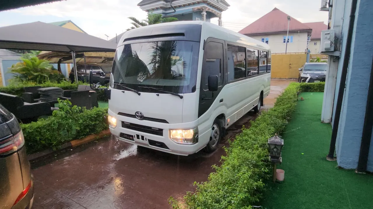 New-model white Toyota Coaster bus with headlights on, front three-quarter view in Lagos